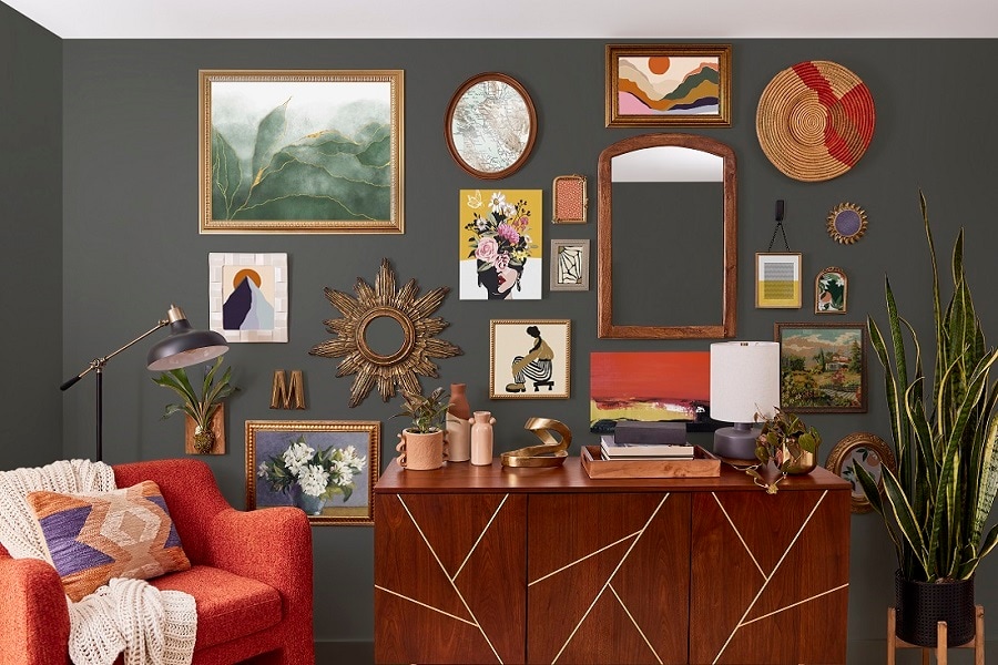 Salon avec mur sombre, art encadré et miroirs accrochés avec des bandes Command. Un buffet en bois, un fauteuil rouge et une grande plante complètent le décor chic.
