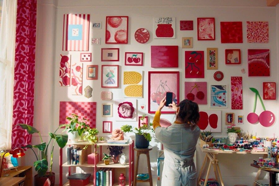 Salon avec mur sombre, art encadré et miroirs accrochés avec des bandes Command. Un buffet en bois, un fauteuil rouge et une grande plante complètent le décor chic.
