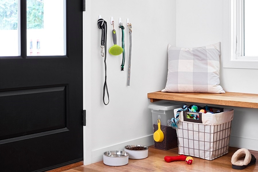Entrée ordonnée avec crochets Command tenant une laisse, une brosse et un collier pour chien. En dessous, des gamelles, un bac de rangement et un panier à jouets. Un banc rembourré au-dessus.
